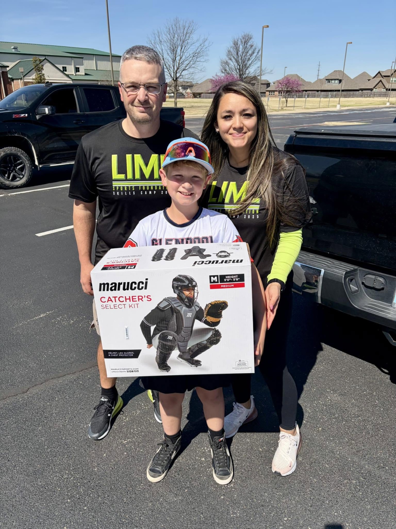 A young baseball player holding a new catcher’s gear kit with two LIME representatives